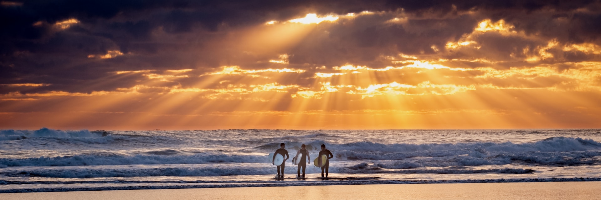 photo - three surfers walking towards the ocean at the best time to surf with beautiful clouds covering late afternoon sun