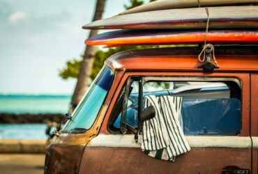 photo - a van parked next to a hawaii beach with surfboards stacked on top, showing value of cost of surfing for those travelling in hawaii