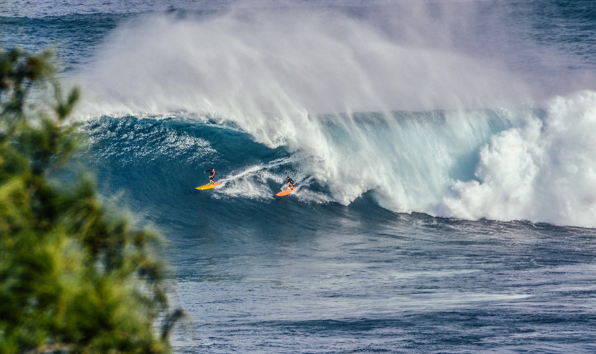 photo - a huge wave in hawaii with two surfers riding it