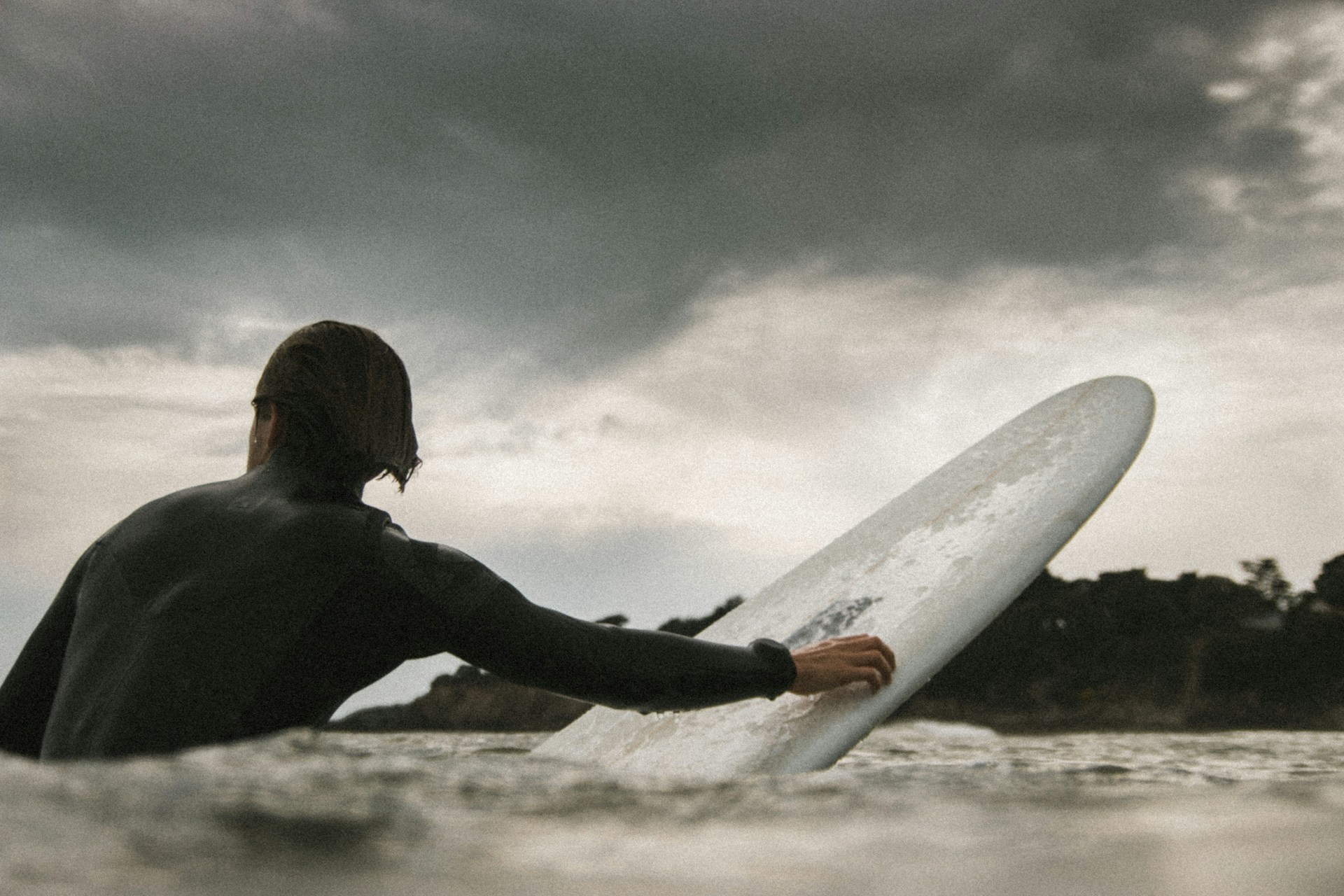 photo - a surfer holding onto his surfboard, wondering about the best time to surf as he is looking at grey clouds son the sky