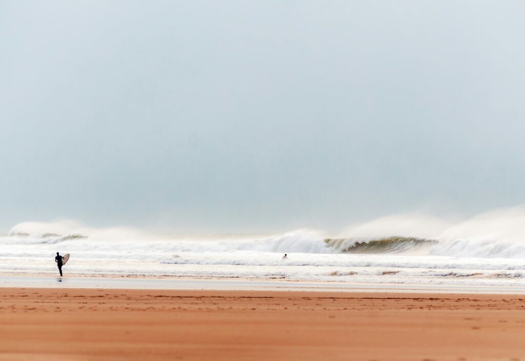 photo - a beach setting with a surfer running towards the ocean with their surf board 