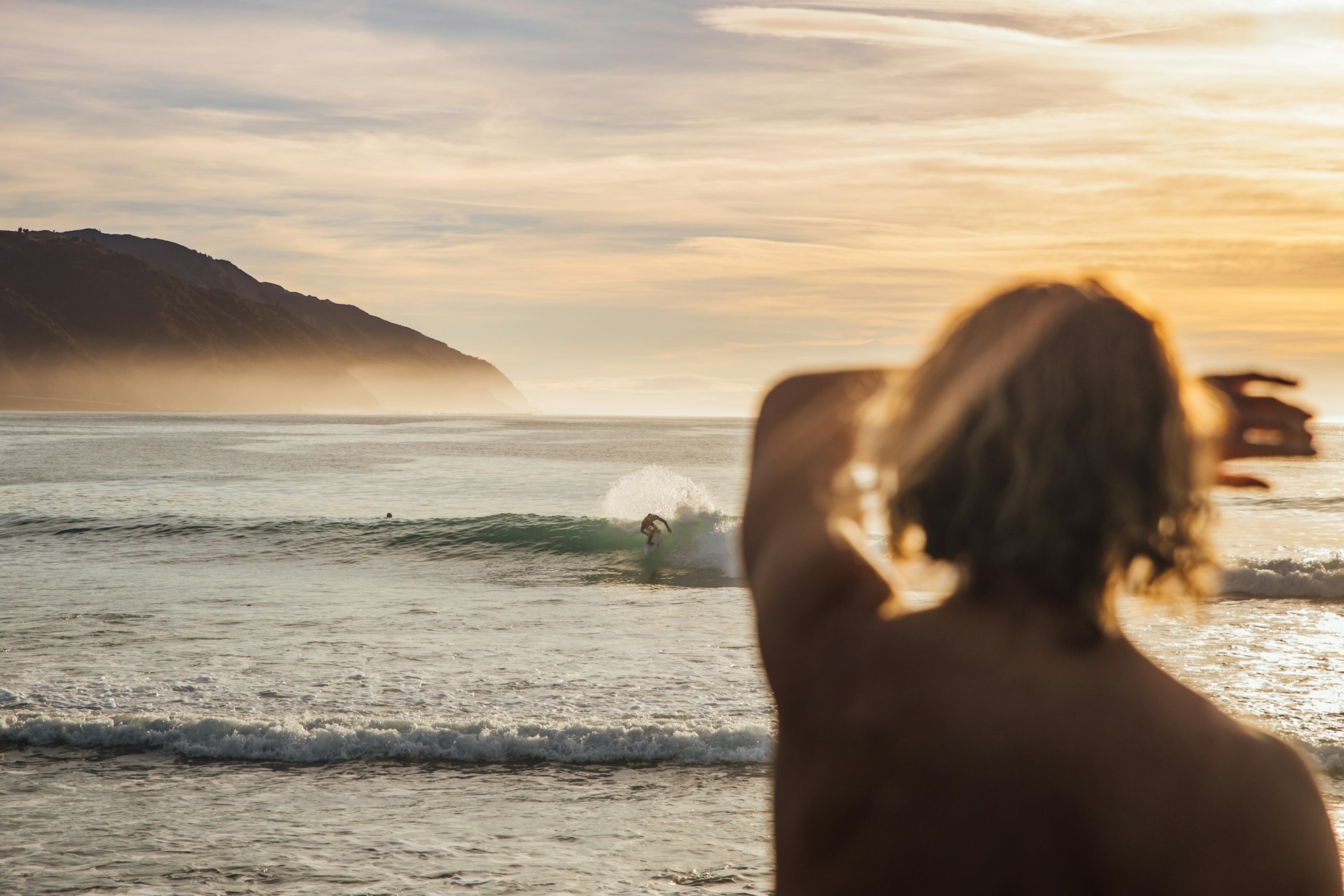 photo - a person looking at the sunrise or sunset at the beach with beautiful view of waves and someone surfing on the Best Surfing in Hawaii for Beginners Waves