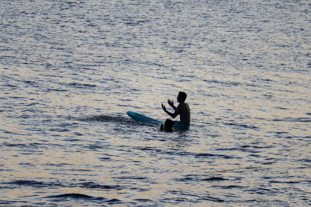 photo - a hawaiian surfer sitting on a surfboard in the ocean waterand performing a spitirual prayer