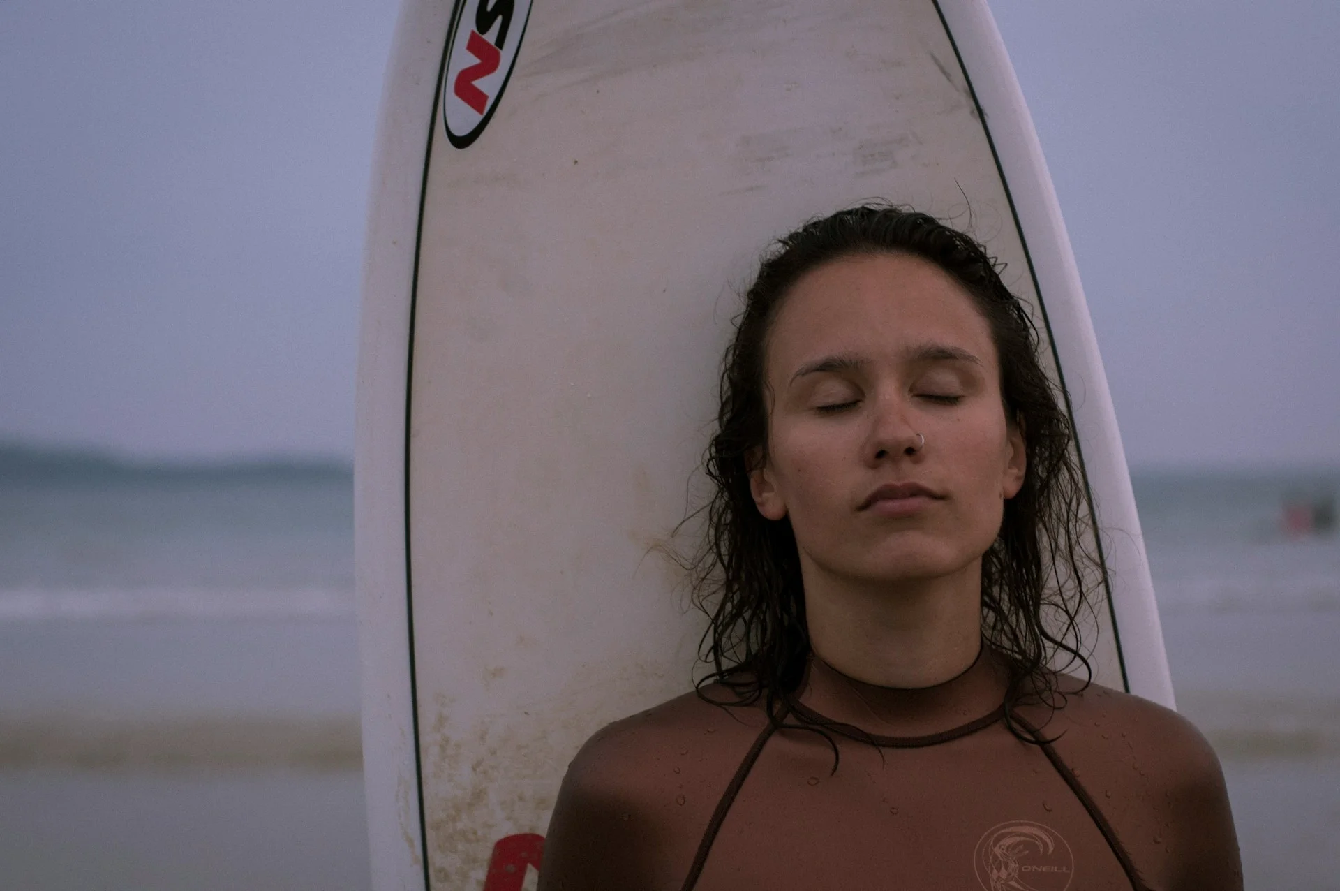 photo - a surfer girl lovingly leaning against hersurf board after using surfing as therapy