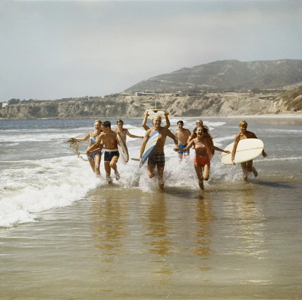 photo - different surfer type running together on the beach 